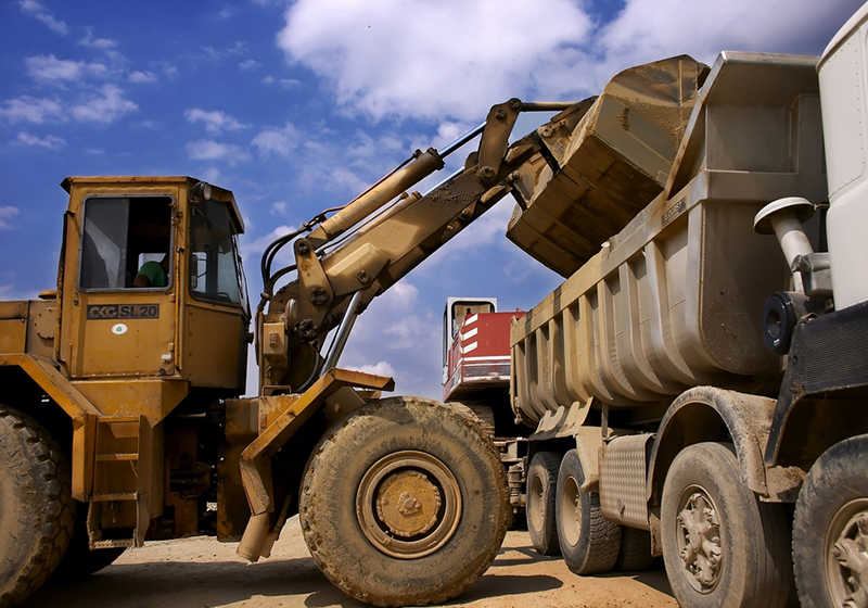 Photo of a construction vehicle putting debris in a dump truck.